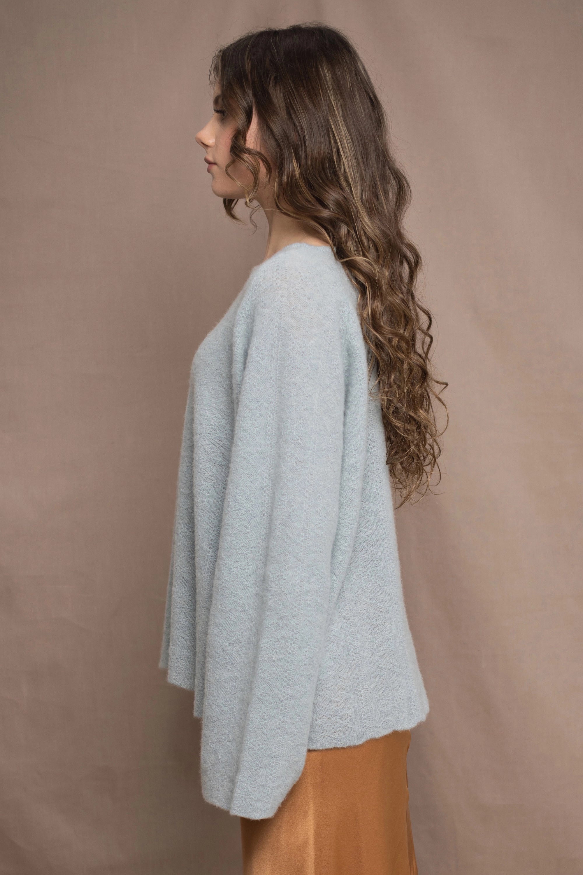 A woman wears a lightweight pointelle cashmere sweater jumper in pale blue turquoise with bronze silk skirt
