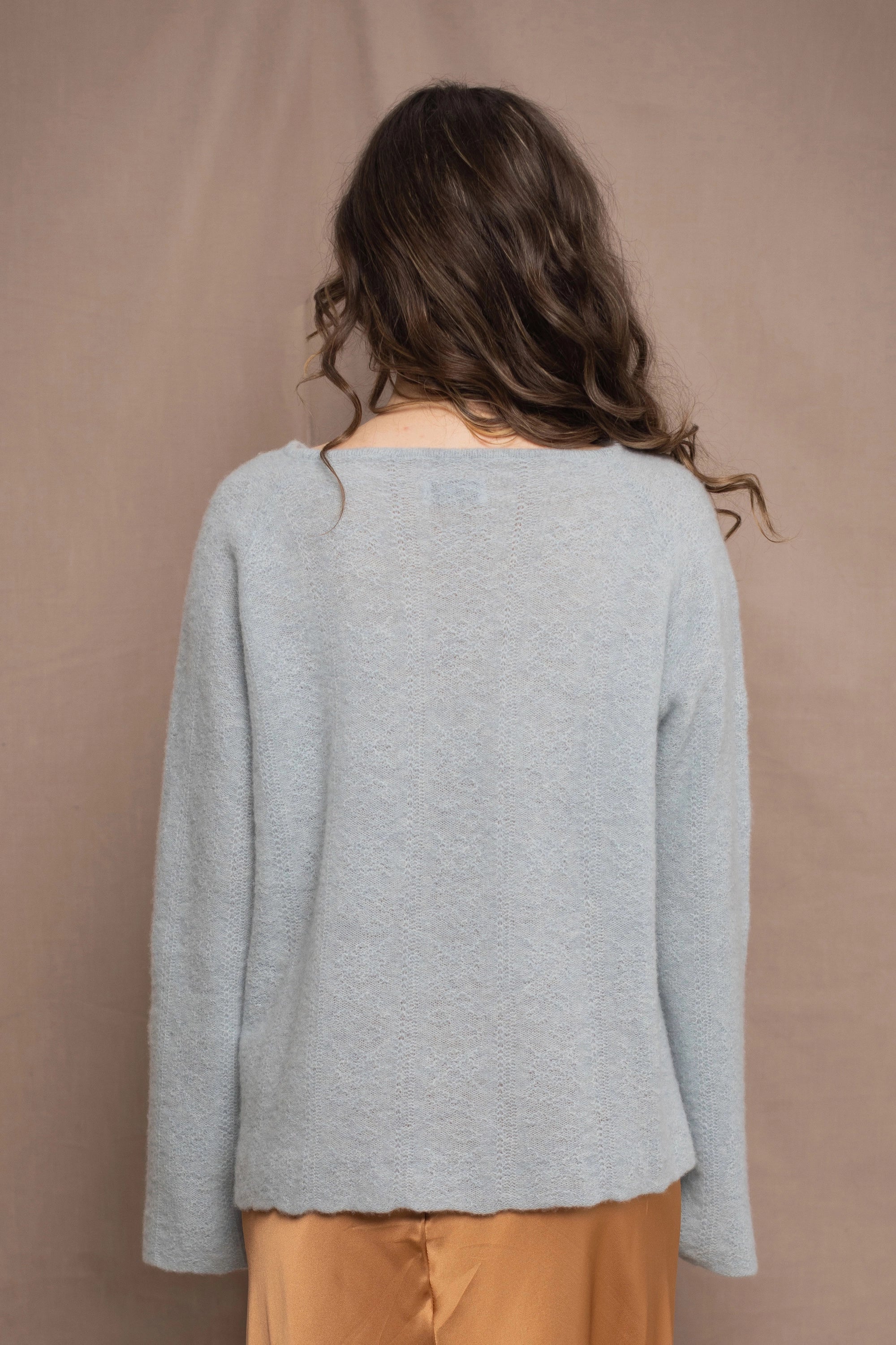 A woman wears a lightweight pointelle cashmere sweater jumper in pale blue turquoise with bronze silk skirt