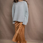 A woman wears a lightweight pointelle cashmere sweater jumper in pale blue turquoise with bronze silk skirt
