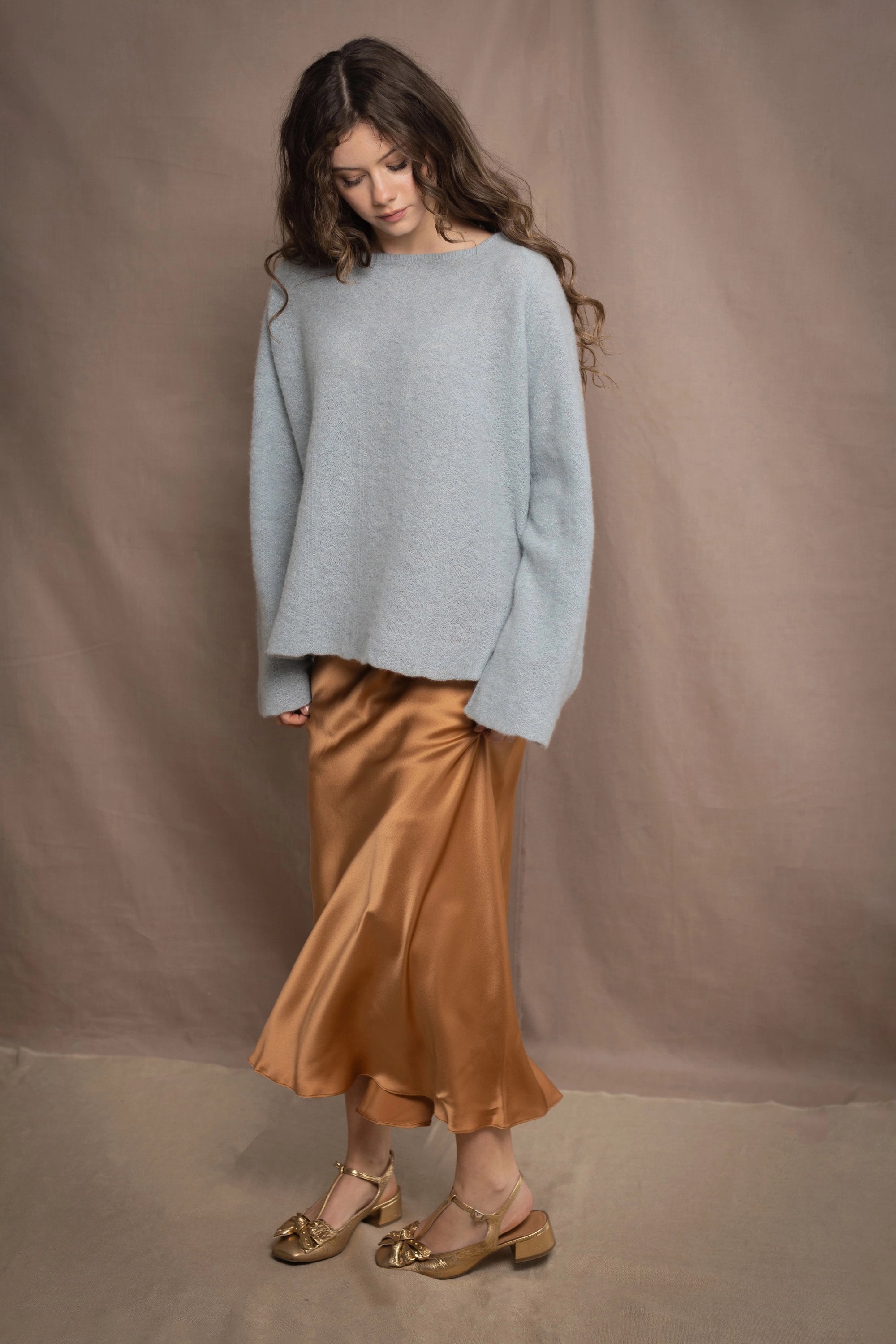 A woman wears a lightweight pointelle cashmere sweater jumper in pale blue turquoise with bronze silk skirt