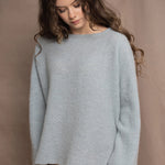A woman wears a lightweight pointelle cashmere sweater jumper in pale blue turquoise with bronze silk skirt