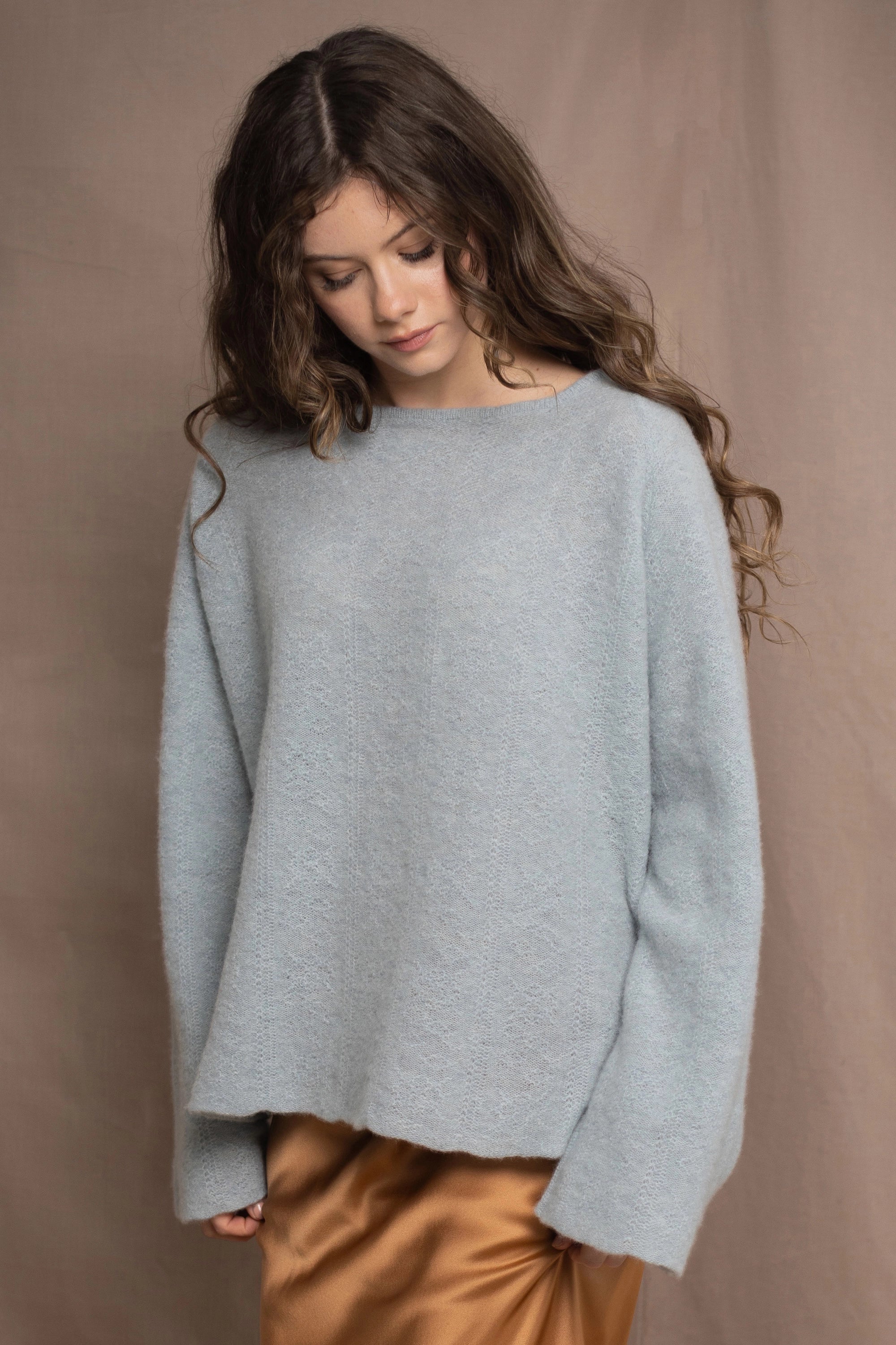 A woman wears a lightweight pointelle cashmere sweater jumper in pale blue turquoise with bronze silk skirt