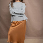 A woman wears a lightweight pointelle cashmere sweater jumper in pale blue turquoise with bronze silk skirt