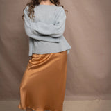 A woman wears a lightweight pointelle cashmere sweater jumper in pale blue turquoise with bronze silk skirt