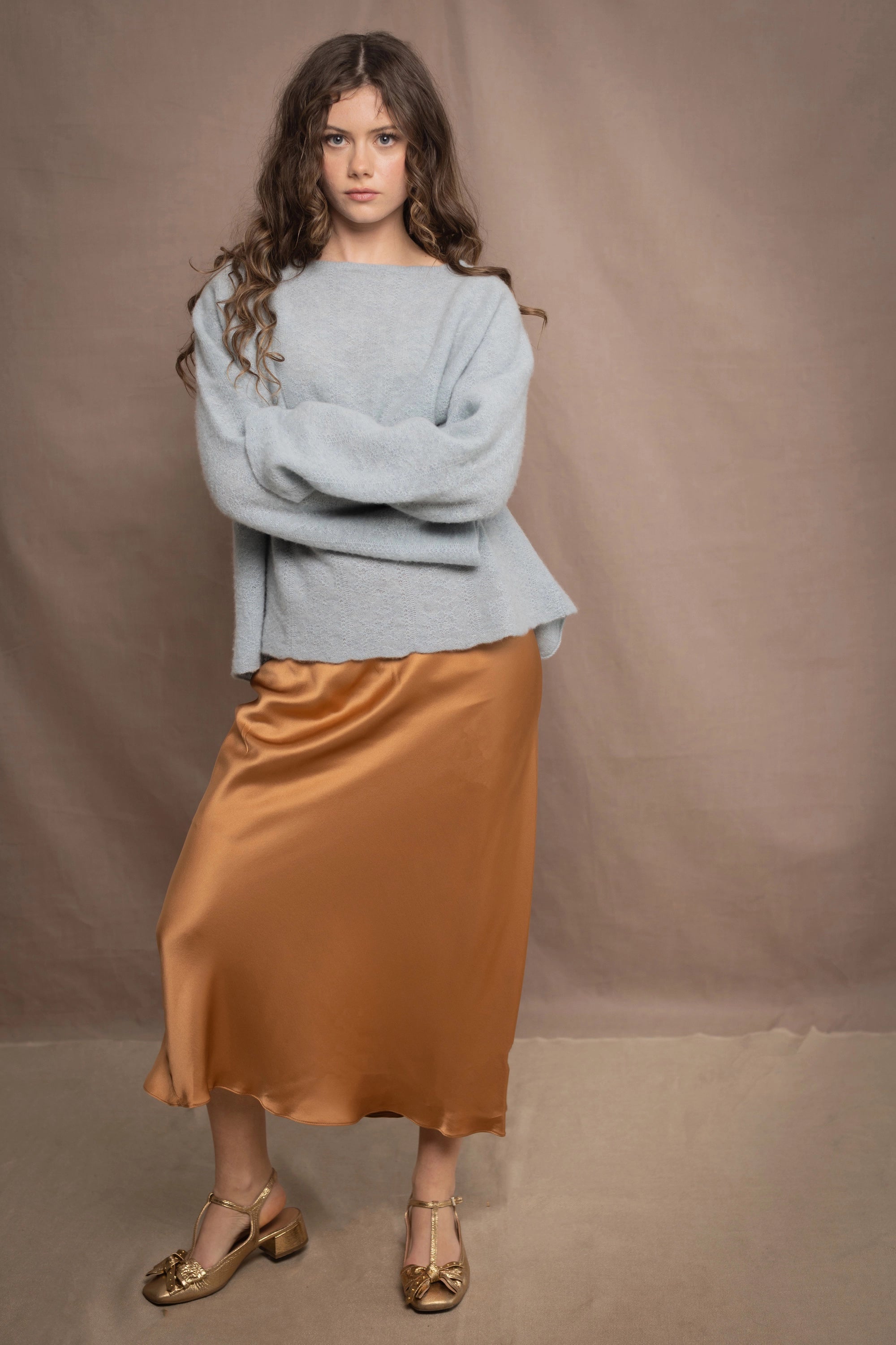 A woman wears a lightweight pointelle cashmere sweater jumper in pale blue turquoise with bronze silk skirt