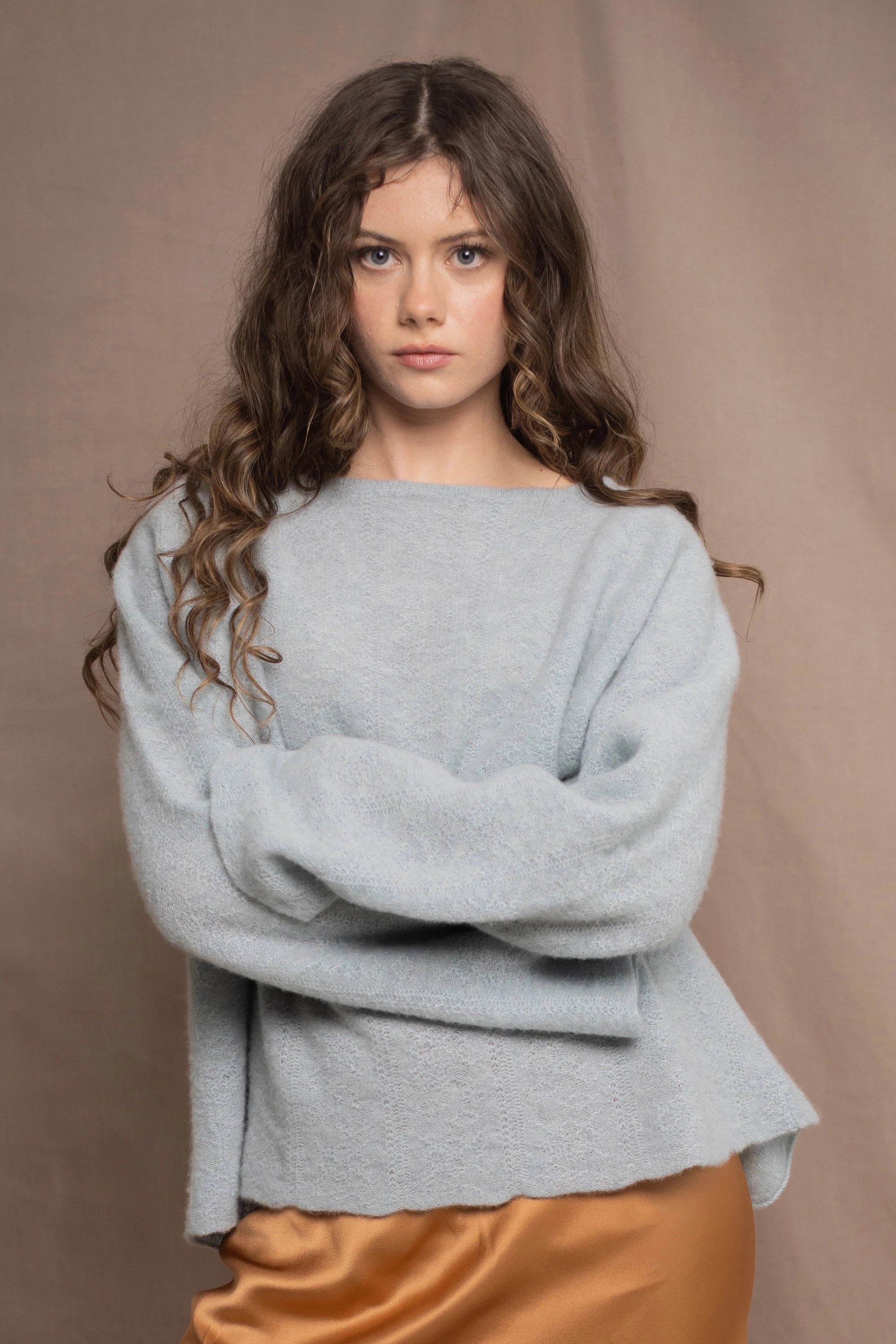 A woman wears a lightweight pointelle cashmere sweater jumper in pale blue turquoise with bronze silk skirt