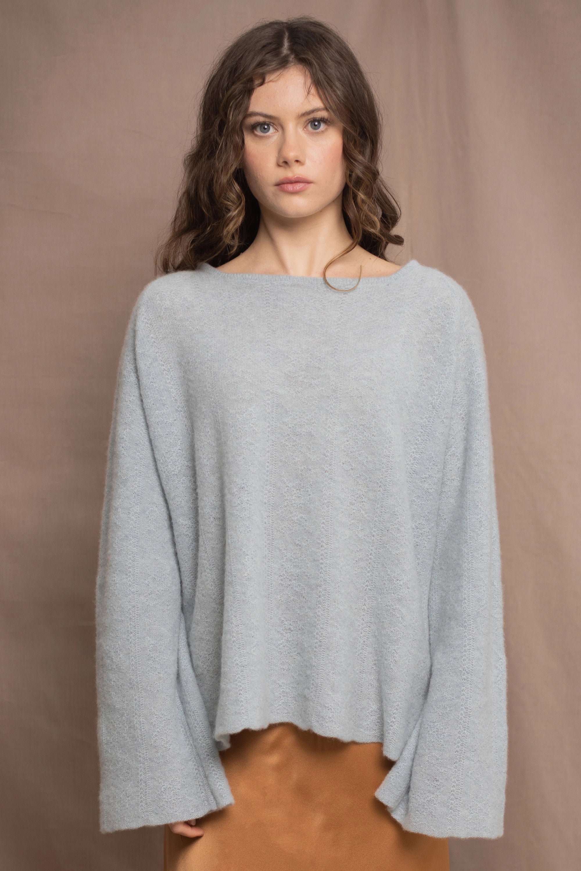 A woman wears a lightweight pointelle cashmere sweater jumper in pale blue turquoise with bronze silk skirt