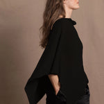 a woman wears a black cashmere cape or poncho over black silk shorts