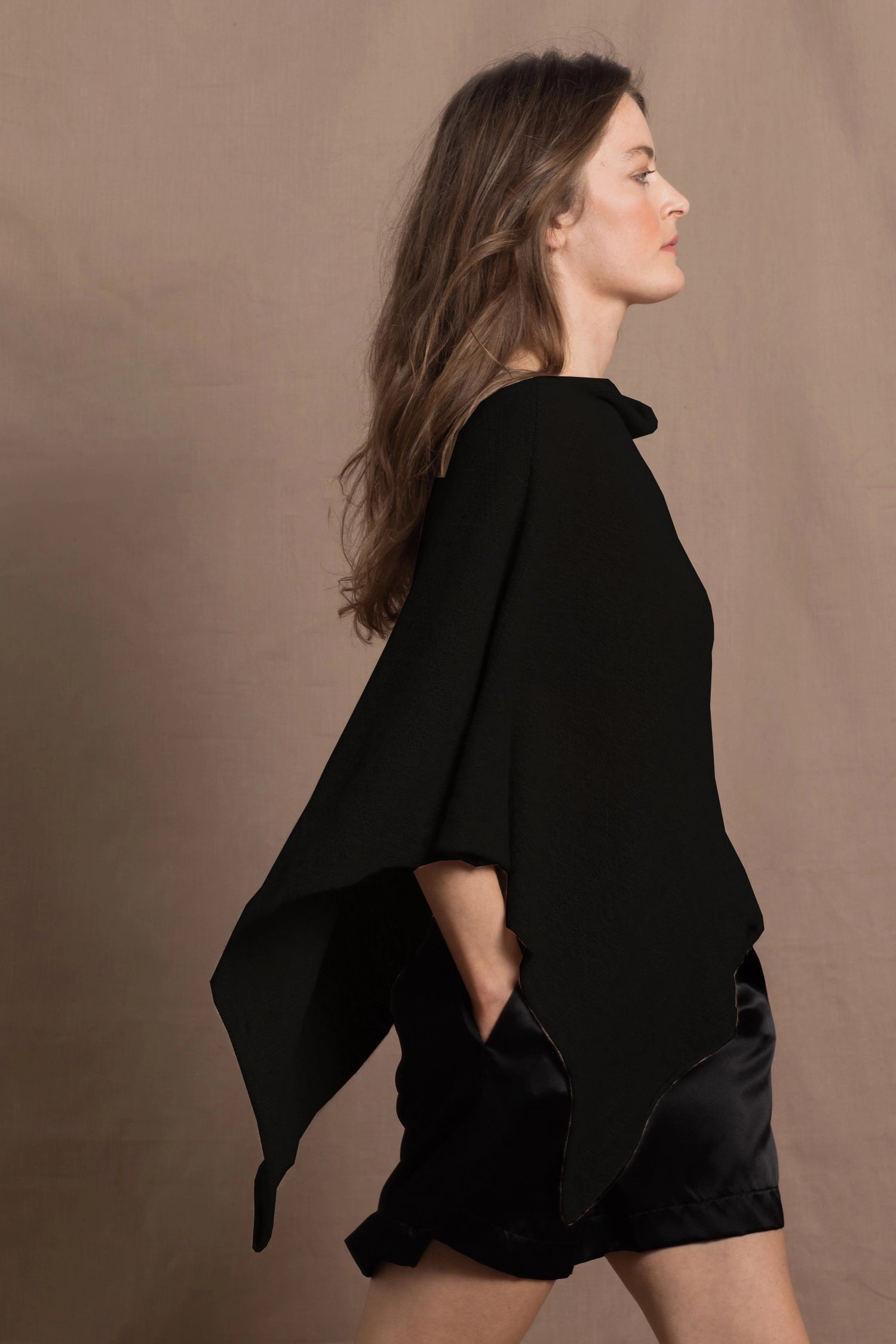 a woman wears a black cashmere cape or poncho over black silk shorts