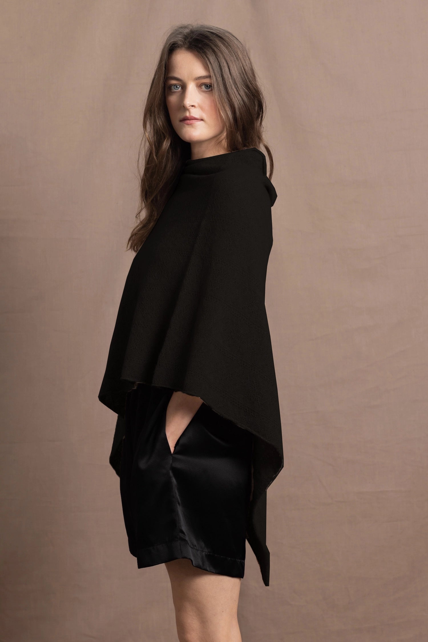 a woman wears a black cashmere cape or poncho over black silk shorts