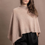 a woman wears a sand coloured cashmere cape or poncho over black silk shorts