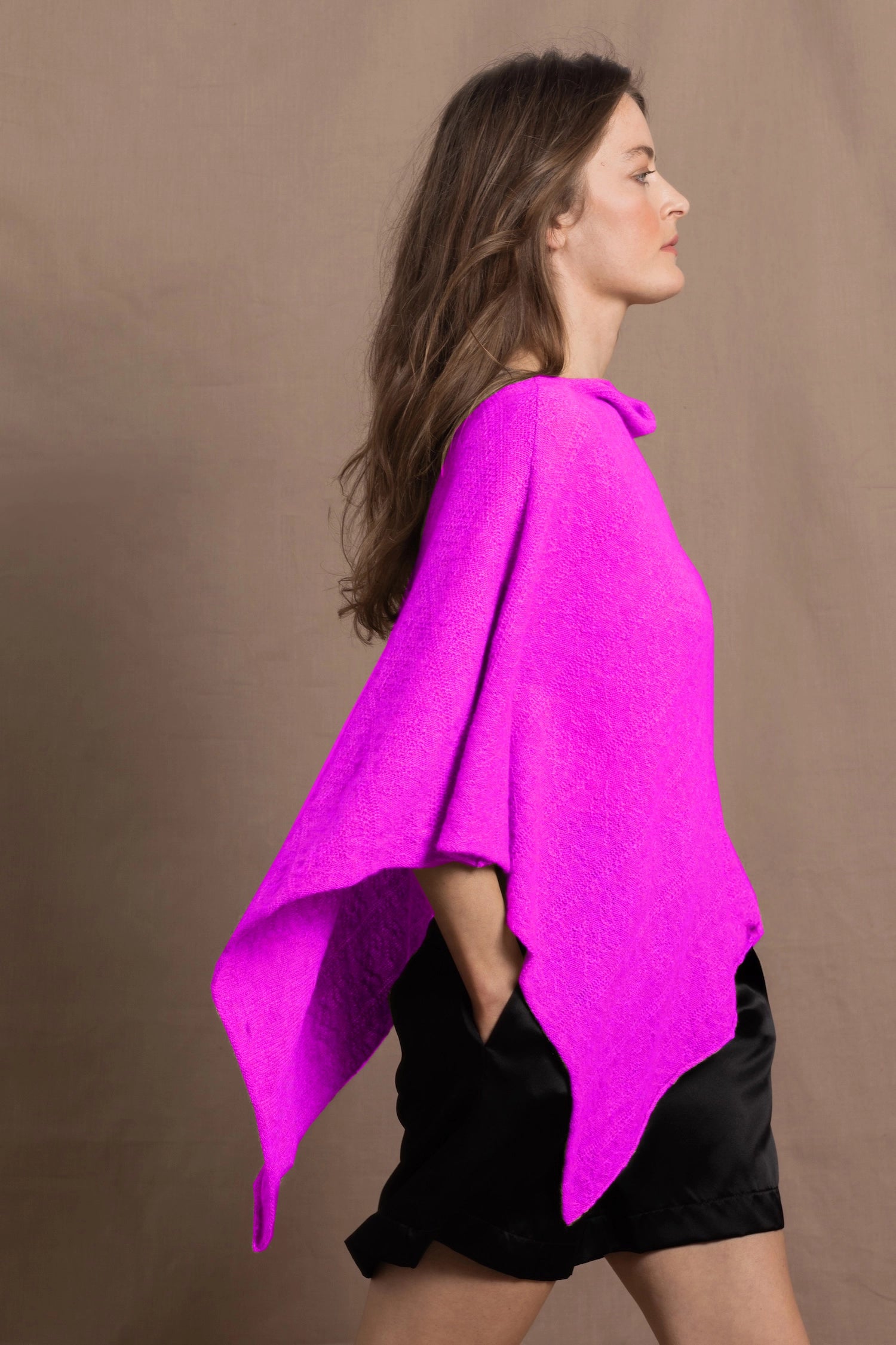 A woman wears a cashmere cape poncho in neon pink with black silk shorts