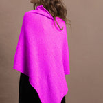 A woman wears a cashmere cape poncho in neon pink with black silk shorts
