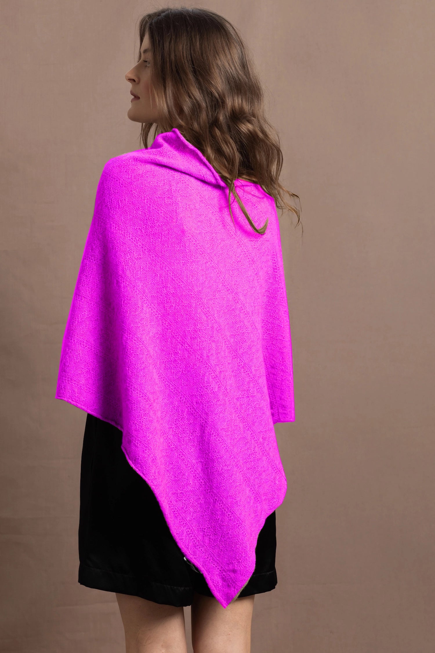 A woman wears a cashmere cape poncho in neon pink with black silk shorts
