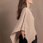 a woman wears a sand coloured cashmere cape or poncho over black silk shorts
