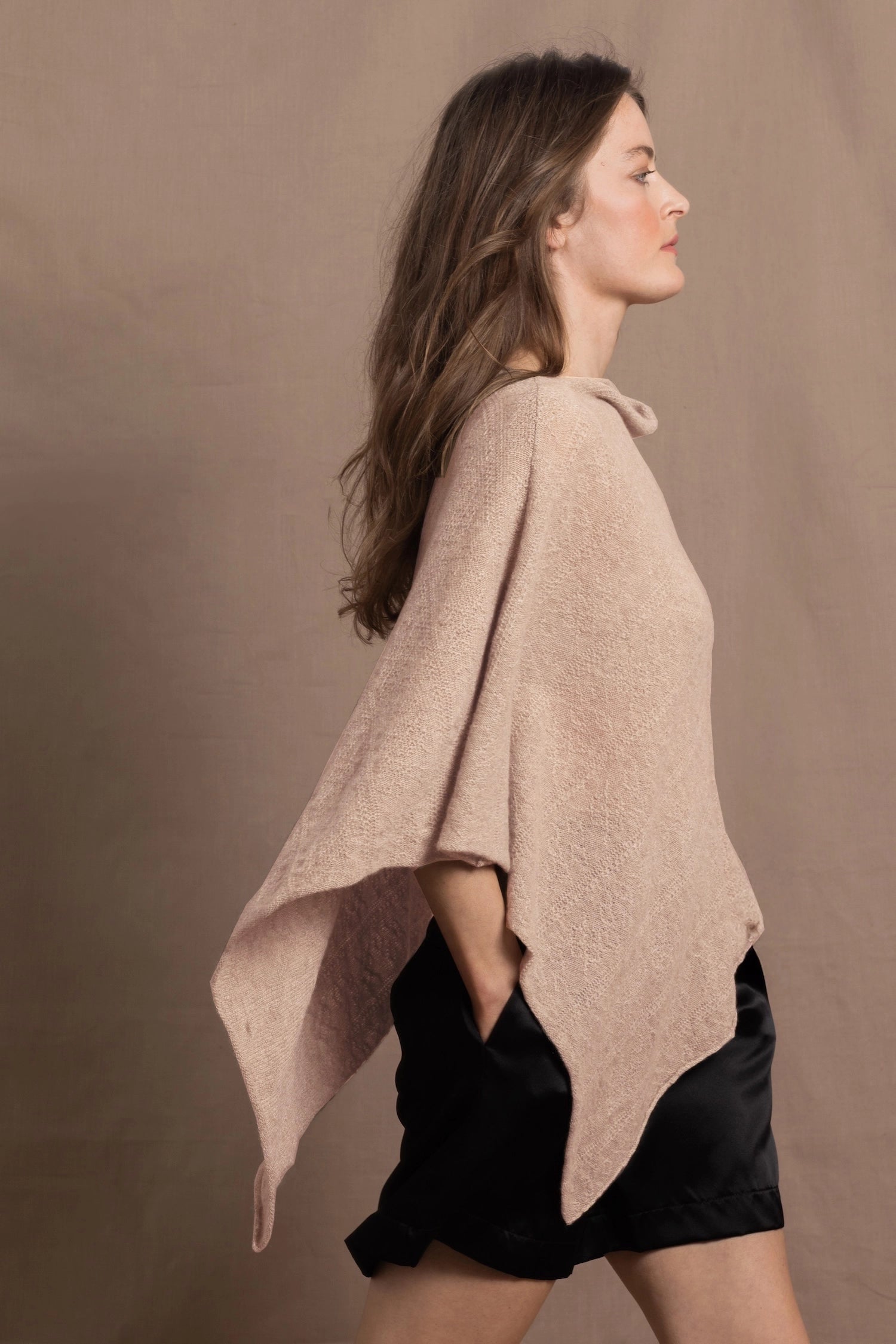 a woman wears a sand coloured cashmere cape or poncho over black silk shorts