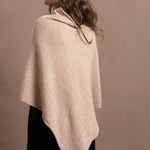 a woman wears a beige coloured cashmere cape or poncho over black silk shorts
