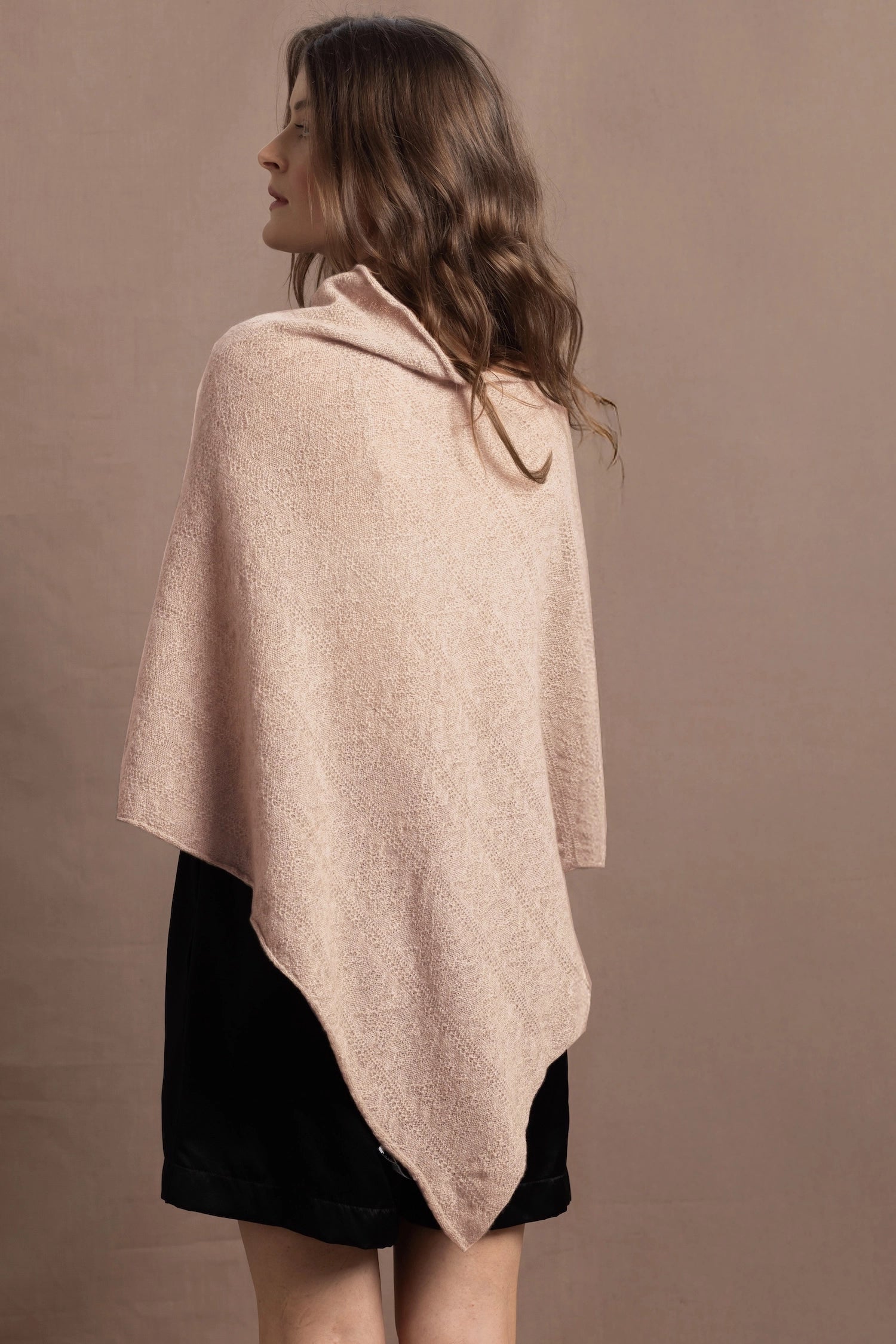 a woman wears a beige coloured cashmere cape or poncho over black silk shorts