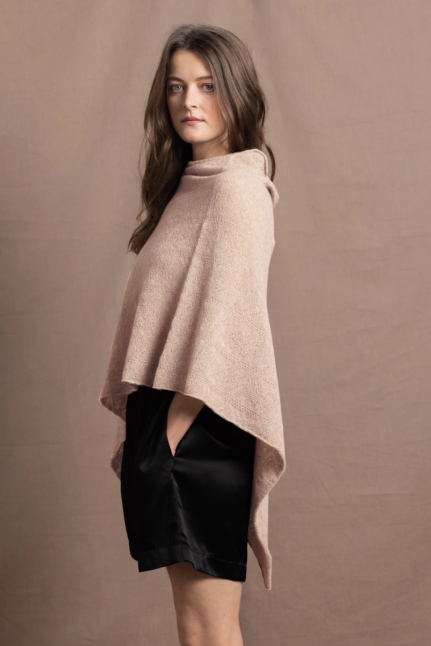 a woman wears a beige coloured cashmere cape or poncho over black silk shorts