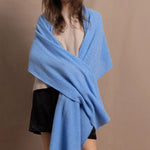 a woman wears a large cashmere shawl wraparound her shoulders in cerulean blue