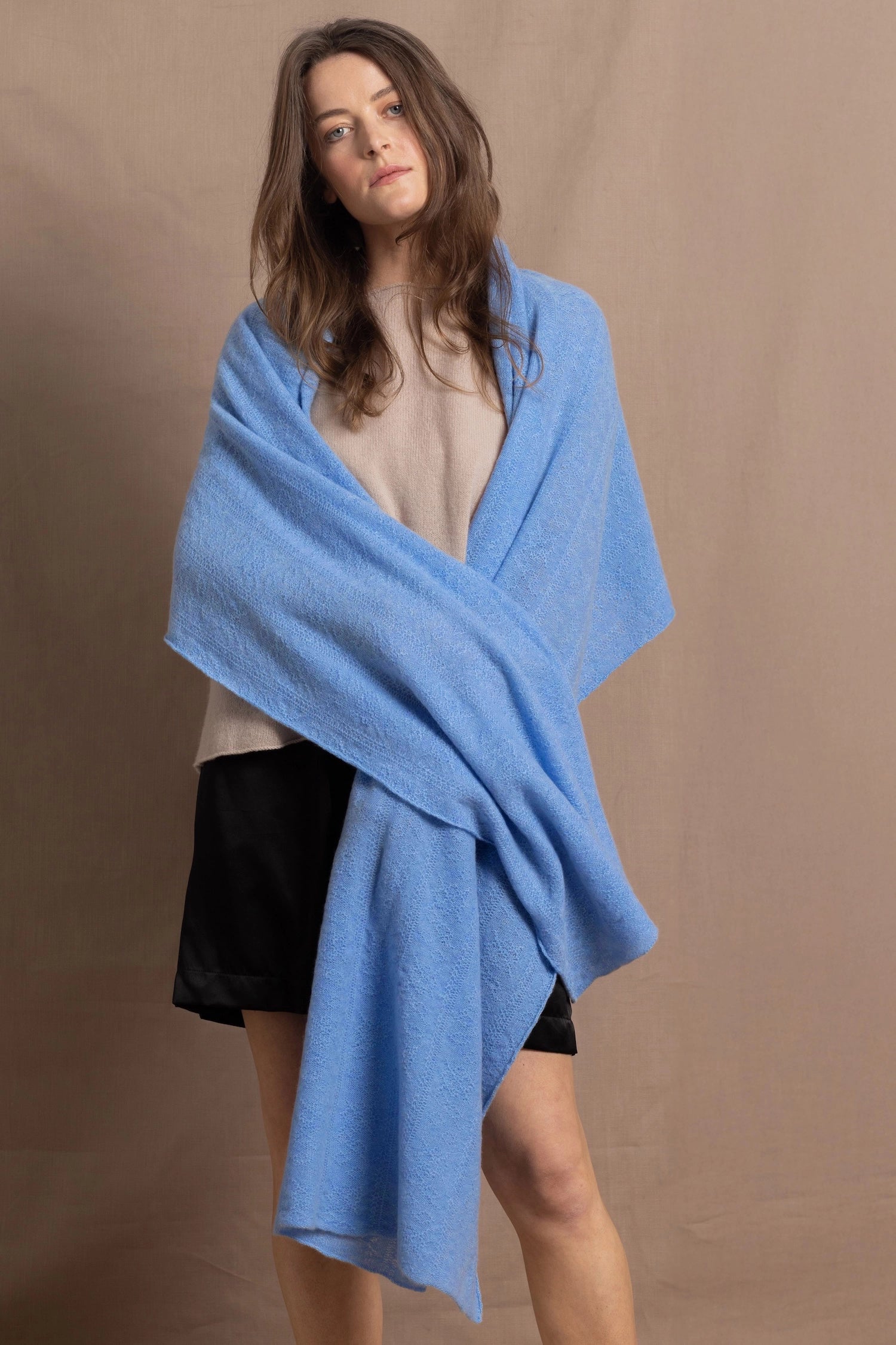 a woman wears a large cashmere shawl wraparound her shoulders in cerulean blue