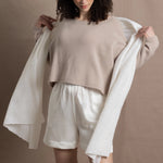 A woman wears a cropped cashmere sweater in beige with white silk shorts and matching cashmere wrap shawl