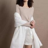A lady wears a pure cashmere pointelle wrap in white over a beige cropped cashmere sweater and white silk shorts
