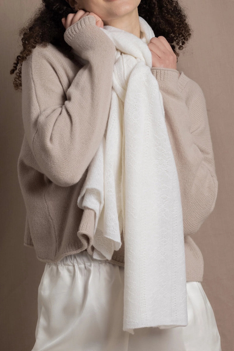A lady wears a pure cashmere pointelle wrap in white over a beige cropped cashmere sweater and white silk shorts