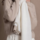 A lady wears a pure cashmere pointelle wrap in white over a beige cropped cashmere sweater and white silk shorts