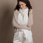 A lady wears a pure cashmere pointelle wrap in white over a beige cropped cashmere sweater and white silk shorts