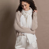 A lady wears a pure cashmere pointelle wrap in white over a beige cropped cashmere sweater and white silk shorts