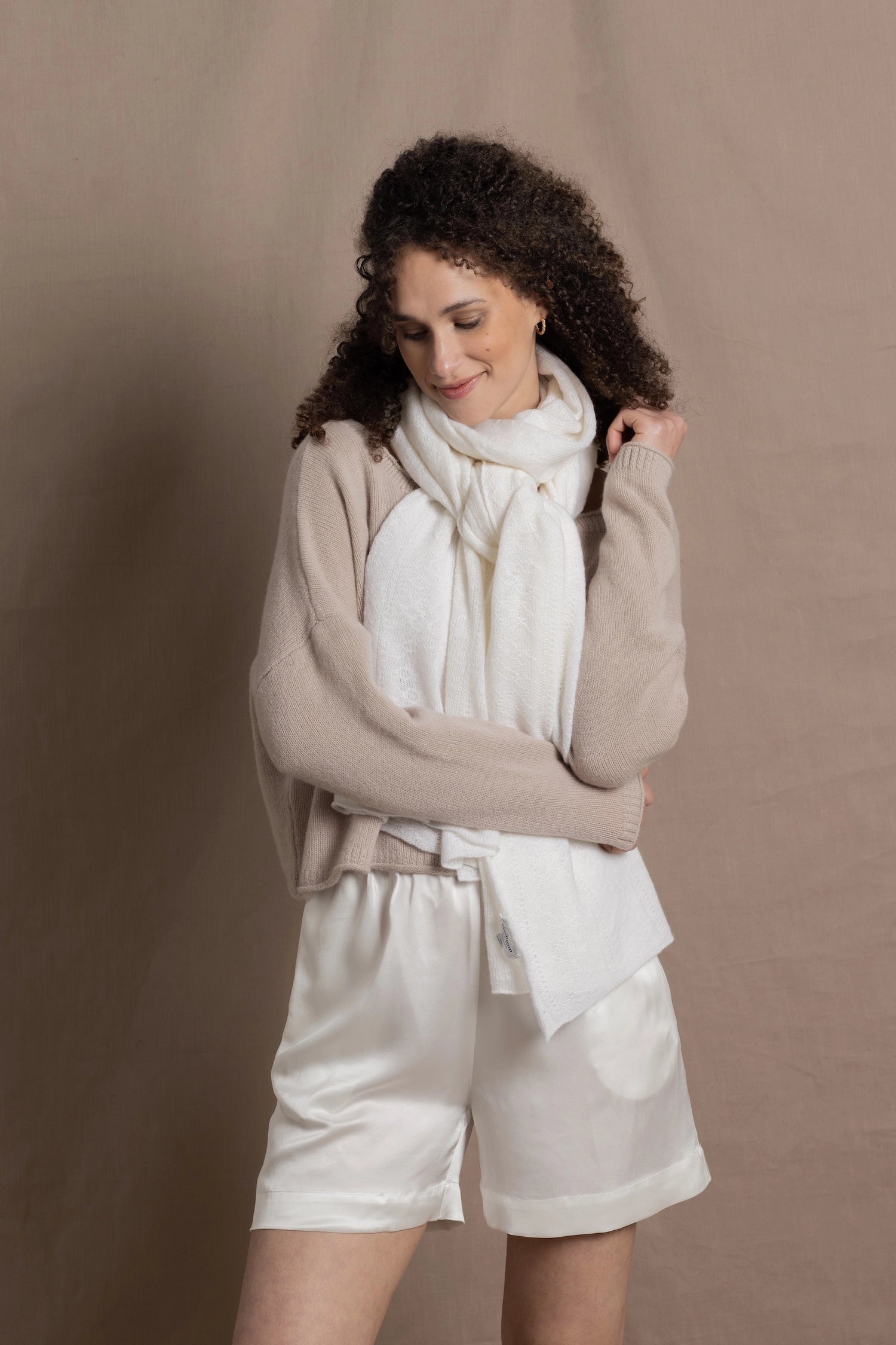 A lady wears a pure cashmere pointelle wrap in white over a beige cropped cashmere sweater and white silk shorts