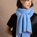 Lady wears a large cashmere scarf in a bright cerulean blue around her neck in a full black silk outfit
