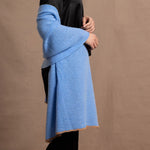 Lady wears a large cashmere wrap shawl in a bright cerulean blue over her shoulders in a full black silk outfit