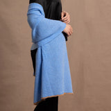 Lady wears a large cashmere wrap shawl in a bright cerulean blue over her shoulders in a full black silk outfit