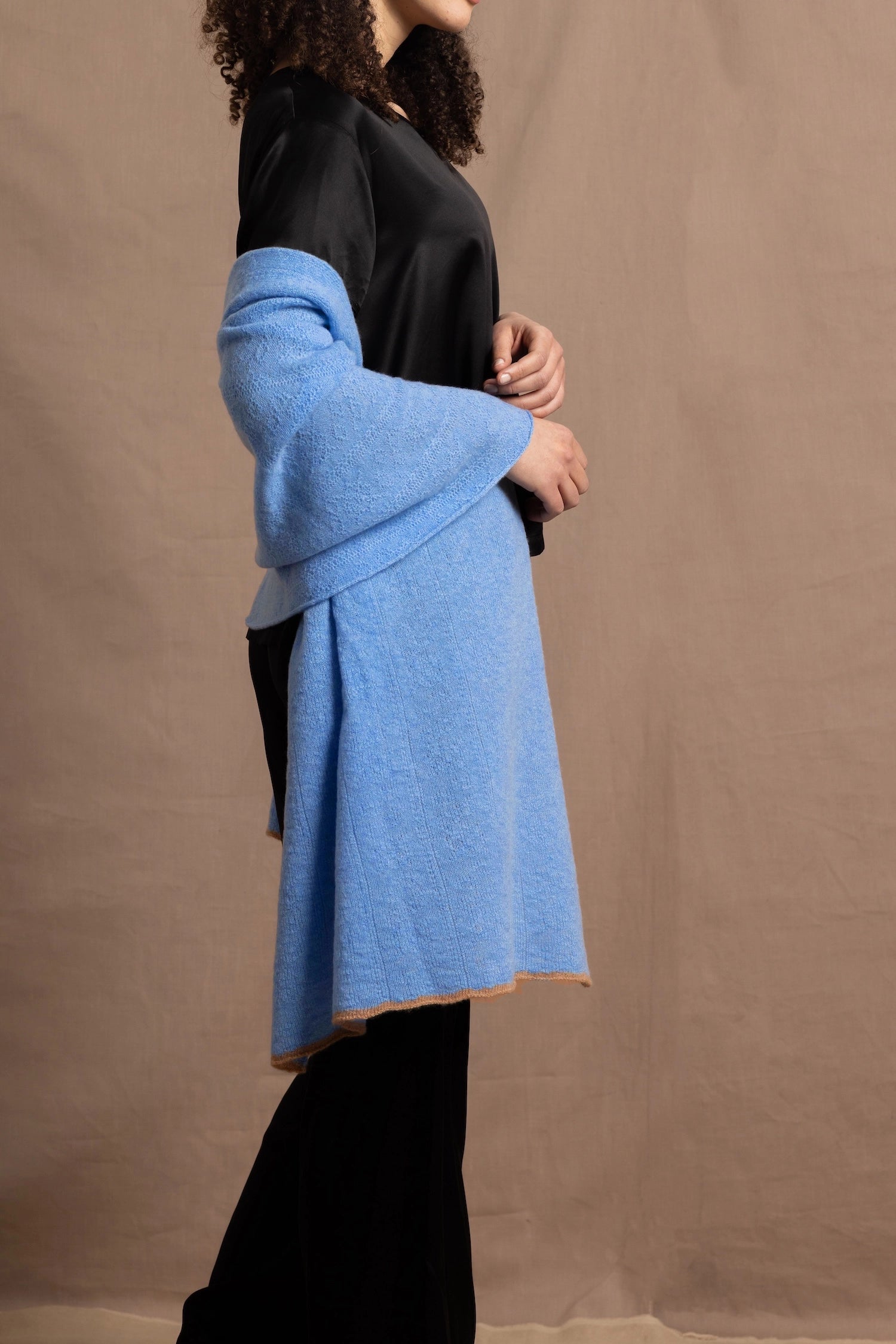 Lady wears a large cashmere wrap shawl in a bright cerulean blue over her shoulders in a full black silk outfit