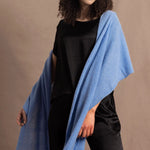 Lady wears a large cashmere wrap shawl in a bright cerulean blue over her shoulders in a full black silk outfit