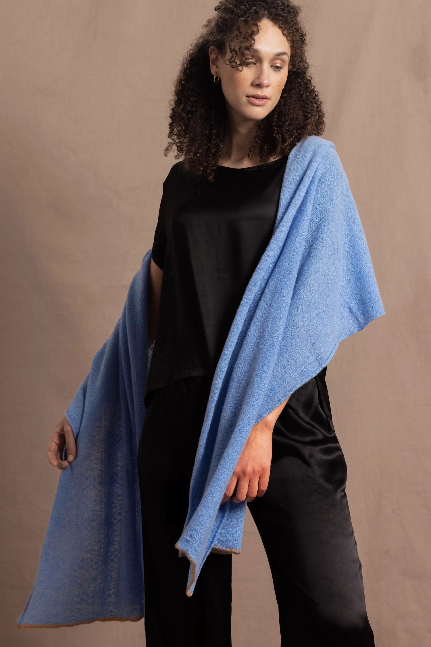 Lady wears a large cashmere wrap shawl in a bright cerulean blue over her shoulders in a full black silk outfit