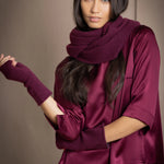 A woman wears a plum burgundy cashmere snood infinity scarf with matching gloves over burgundy silk clothing