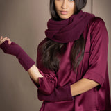 A woman wears a plum burgundy cashmere snood infinity scarf with matching gloves over burgundy silk clothing