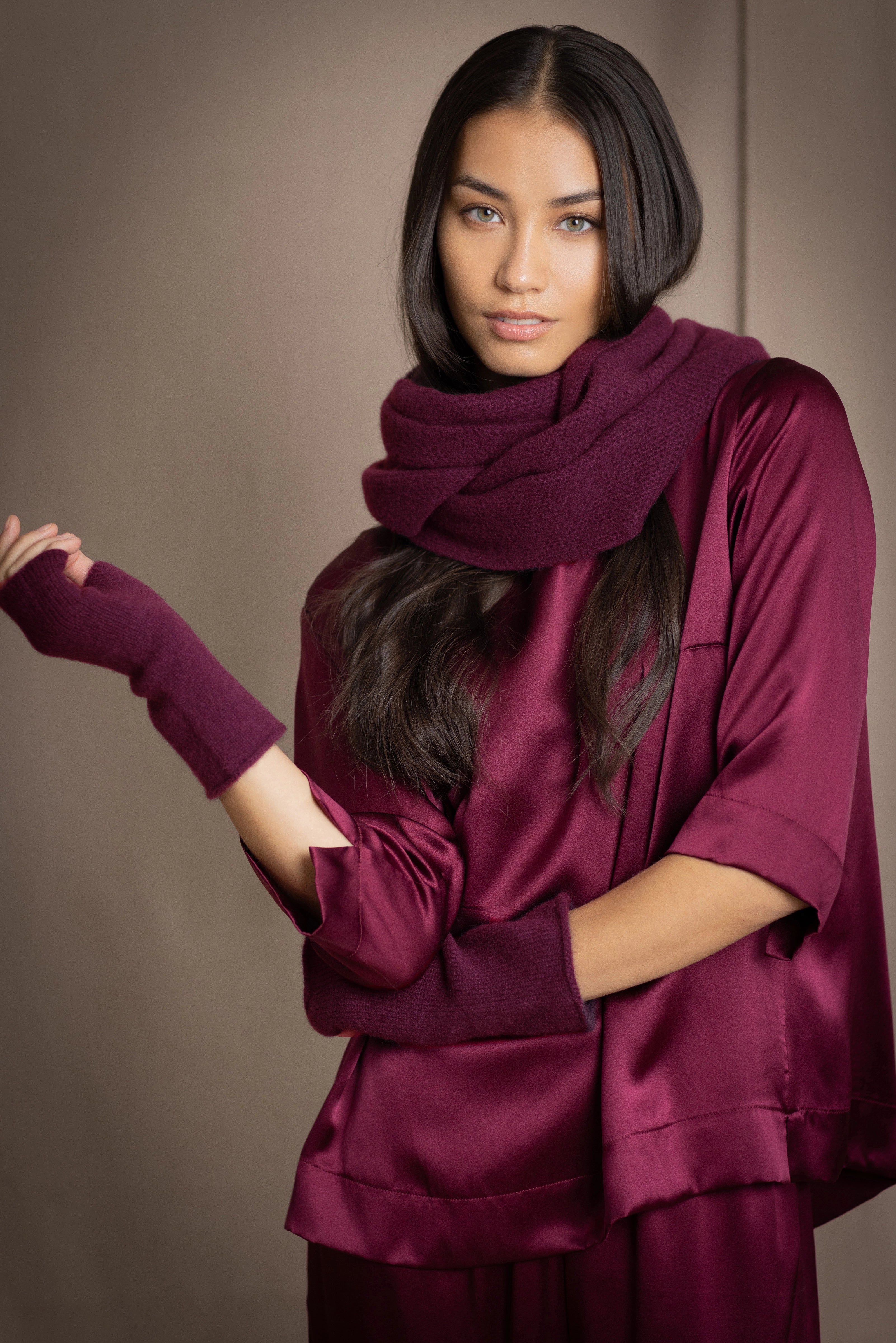 A woman wears a plum burgundy cashmere snood infinity scarf with matching gloves over burgundy silk clothing