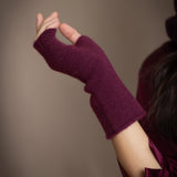A close-up of a person's hand wearing fingerless cashmere gloves in deep plum burgundy
