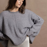 A woman wears a pure cashmere sweater that is oversized in grey with a silver skirt