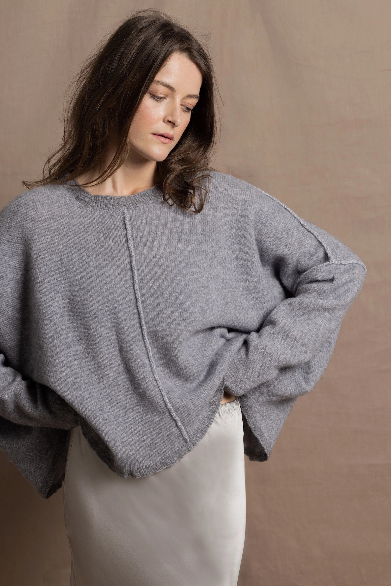 A woman wears a pure cashmere sweater that is oversized in grey with a silver skirt