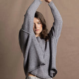 A woman wears a pure cashmere sweater that is oversized in grey with a silver skirt