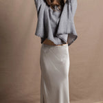 A woman wears a pure cashmere sweater that is oversized in grey with a silver skirt