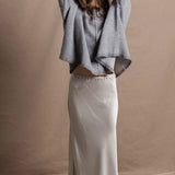 A woman wears a pure cashmere sweater that is oversized in grey with a silver skirt