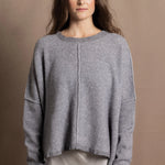 A woman wears a pure cashmere sweater that is oversized in grey with a silver skirt