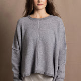 A woman wears a pure cashmere sweater that is oversized in grey with a silver skirt