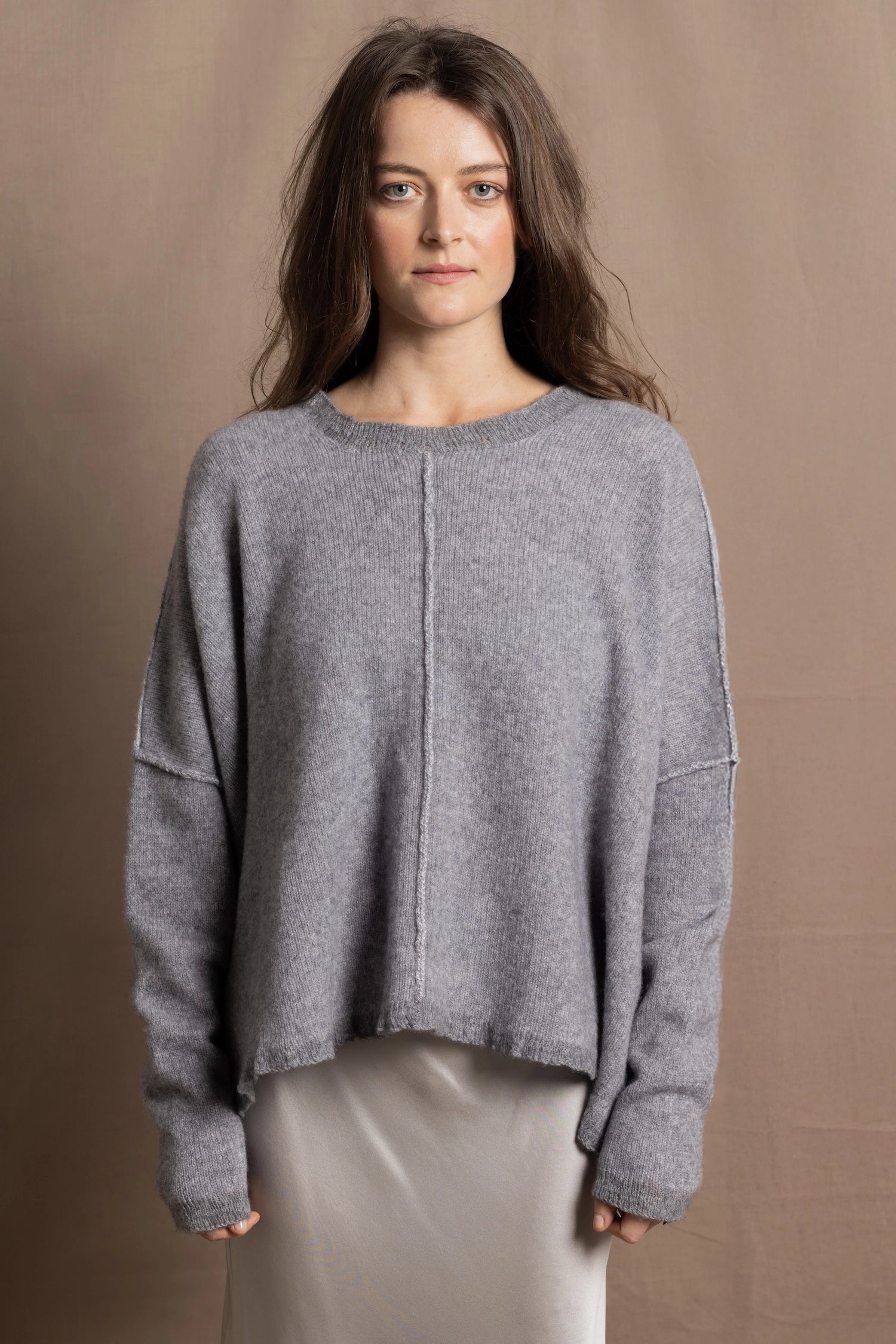 A woman wears a pure cashmere sweater that is oversized in grey with a silver skirt